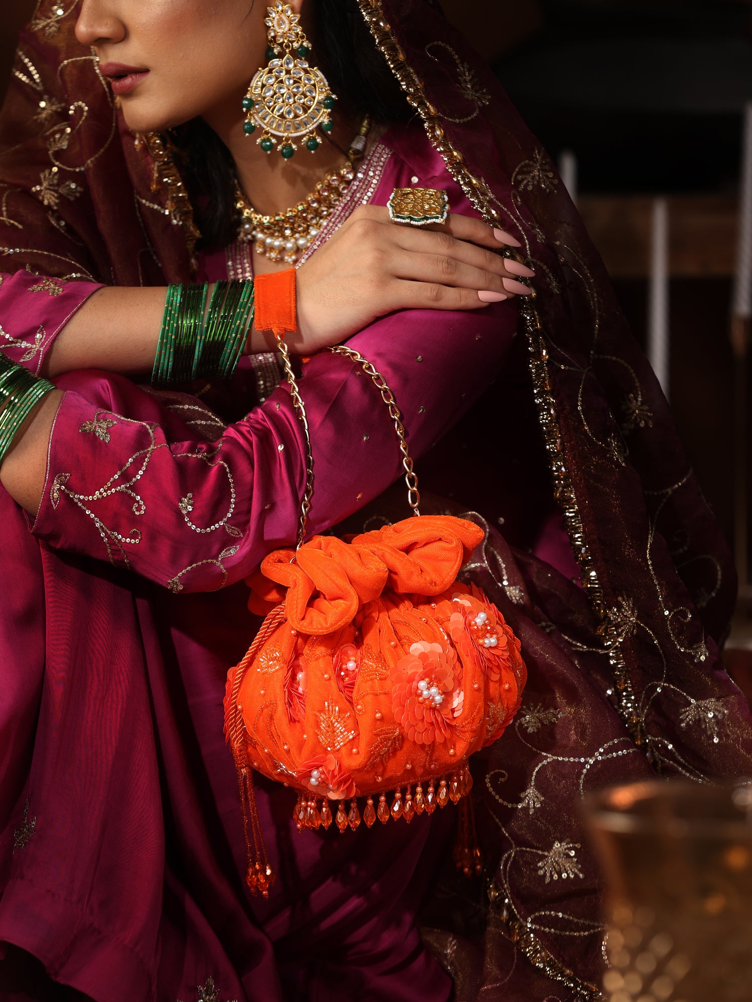 Woman in traditional attire holding an orange bag with jewelry on a dark background